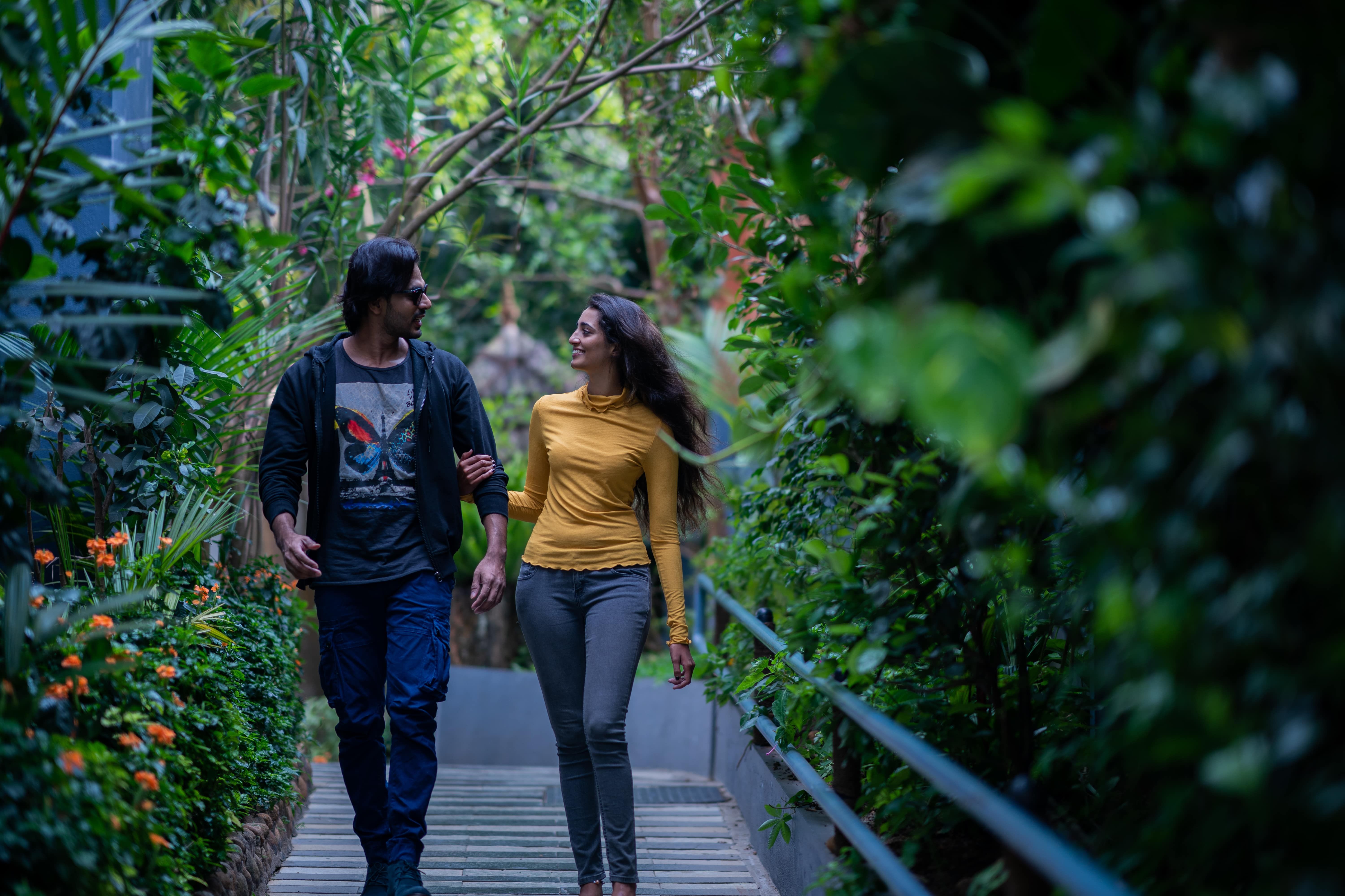 Couple holding hands, walking through a lush, green indoor botanical garden.