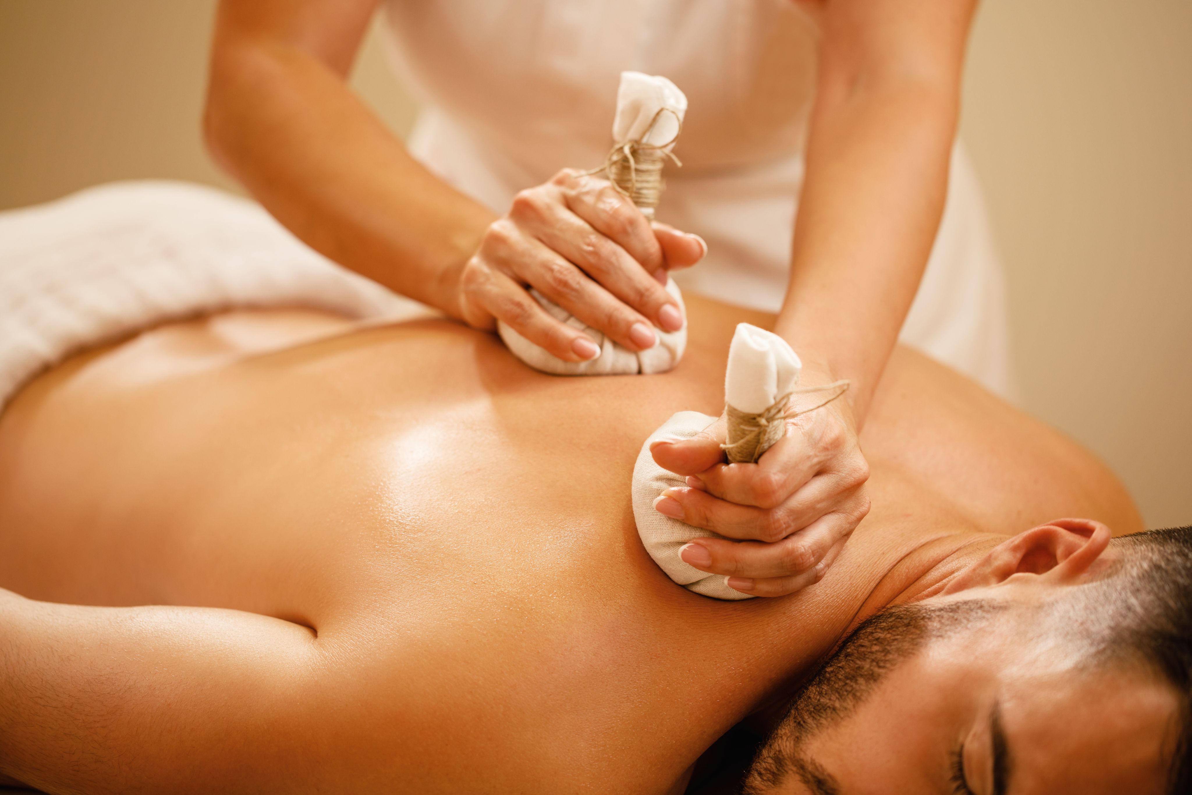 Masseuse using warm herbal compresses on a person's bare back for a relaxing spa treatment.