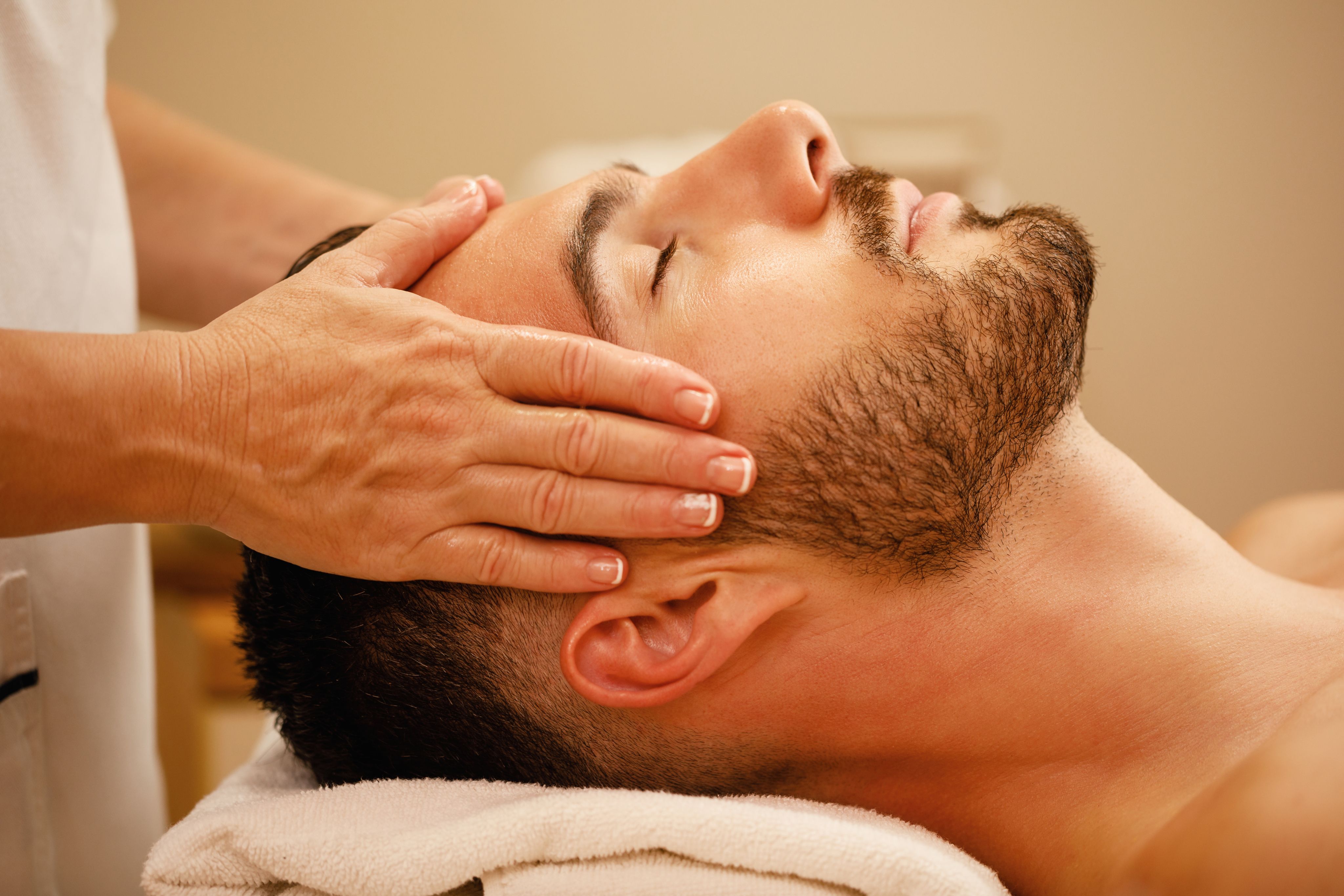 Man with closed eyes receiving a relaxing head massage from a therapist.