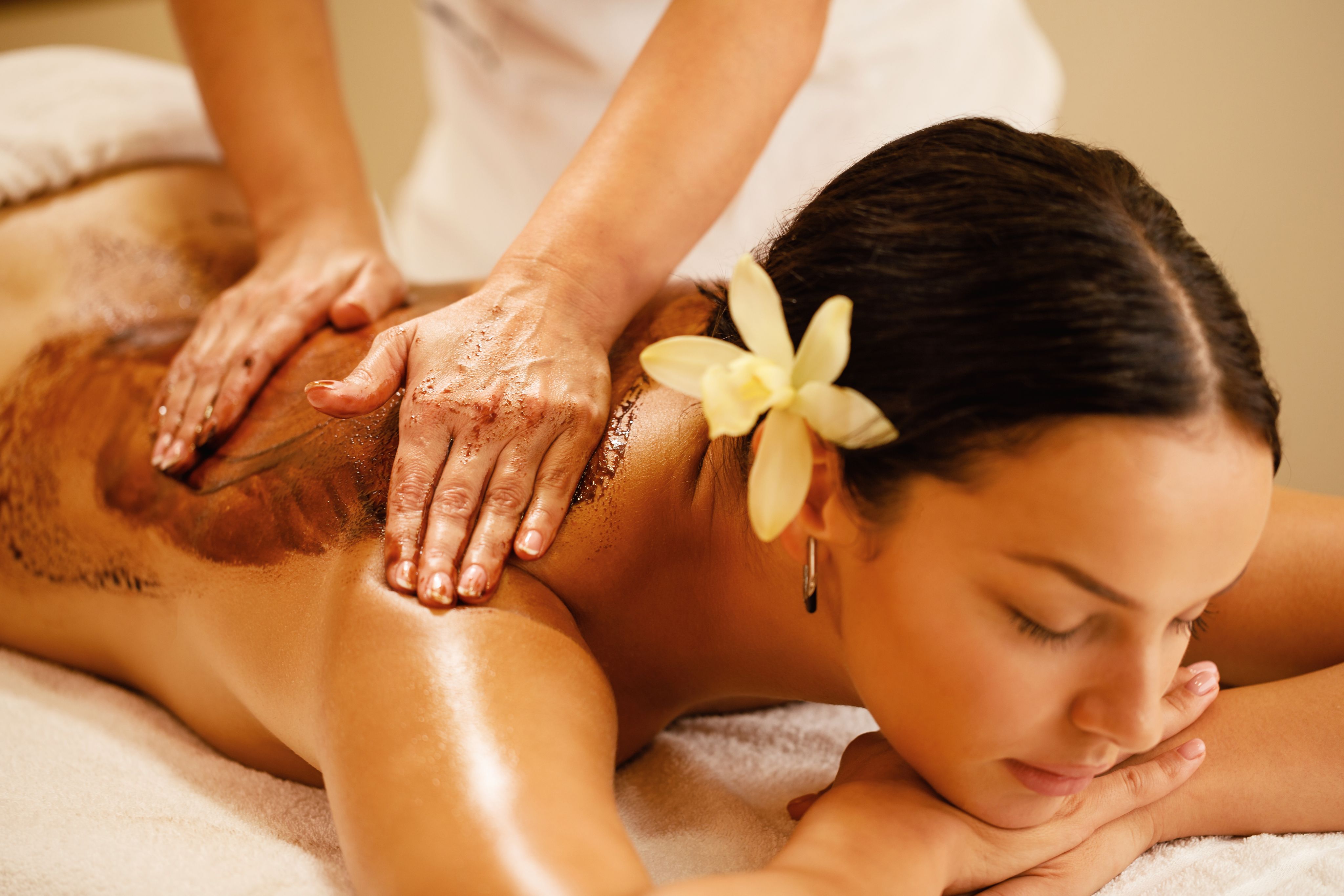 Woman receiving a relaxing back scrub treatment with a therapist's hands applying the scrub.